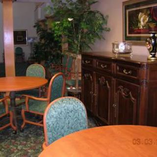 A cozy room with wooden tables, upholstered chairs, a decorative cabinet, and indoor greenery.