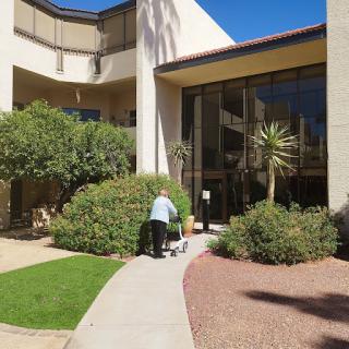 A person pushing a cart along a pathway in front of a well-maintained building surrounded by greenery.