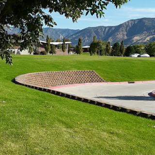 A scenic view of a park featuring a curved brick edge and green grass with mountains in the background.