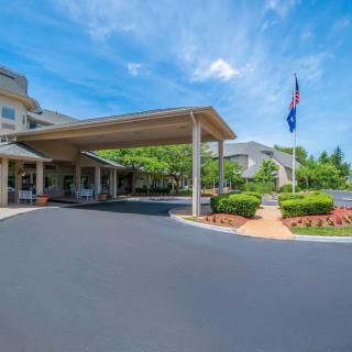 A building entrance with a covered driveway and landscaped surroundings under a clear blue sky.