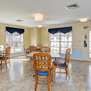 A bright dining area with wooden chairs and tables, featuring large windows that allow ample natural light.
