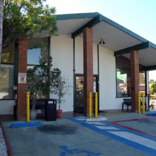 A small drive-thru building with a parking lot and trees around it.