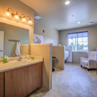 A spacious bathroom with a sink, mirror, and comfortable seating by the window.