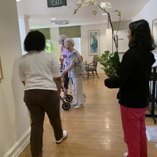 People walking in a nursing home hallway, one person carrying an orchid plant.