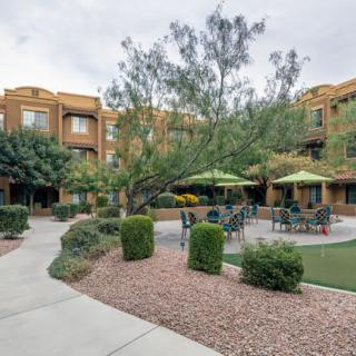 A beautifully landscaped courtyard in an apartment complex featuring outdoor seating and umbrellas.