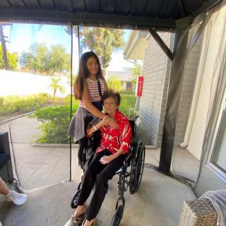 A person in a wheelchair is accompanied by another standing beside them, enjoying time together outdoors.