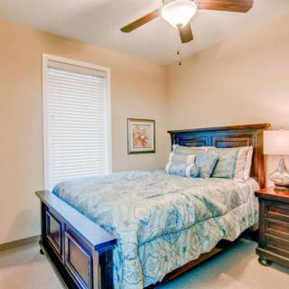 A cozy bedroom with a bed, nightstand, lamp, and ceiling fan.
