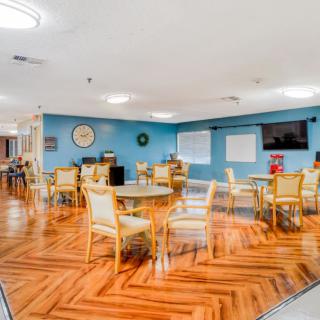 A spacious dining area with wooden flooring, blue walls, and multiple tables and chairs arranged for seating.
