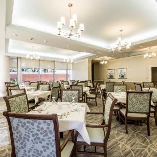 An elegant dining room with neatly arranged tables and chairs, illuminated by chandeliers.