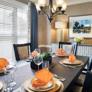 A neatly set dining room table with orange napkins and elegant decor.