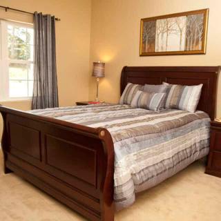 A cozy bedroom featuring a wooden bed frame with striped bedding, accompanied by a window with curtains and a bedside lamp.