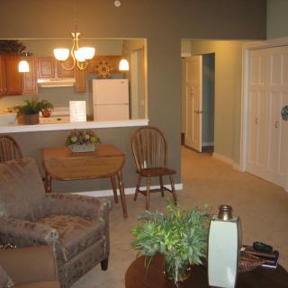 A cozy living room with an open view into the kitchen, featuring comfortable seating and warm lighting.
