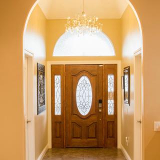 A warmly lit entryway featuring a wooden front door with decorative glass panels and an elegant chandelier.