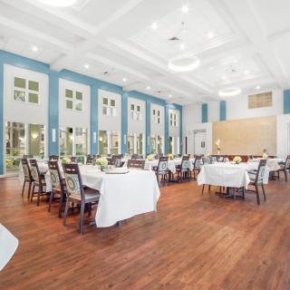 A spacious and elegantly decorated dining room set up with tables and chairs, featuring large windows and bright lighting.