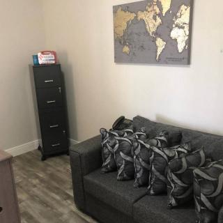A cozy living room with a gray couch and decorative pillows, a world map on the wall, and a tall cabinet in the corner.