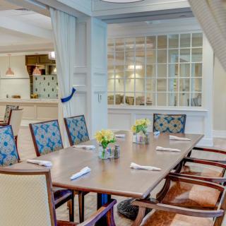 A neatly arranged dining room featuring a wooden table with chairs, adorned with vases of yellow flowers and set with cutlery.