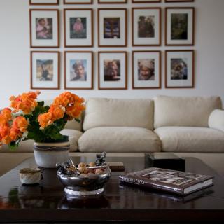 A cozy living room featuring a beige sofa, vibrant orange flowers on a coffee table, and framed artwork on the wall.