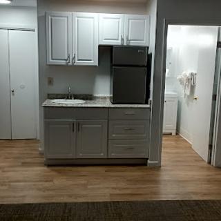 A modern kitchen featuring white cabinets and a stainless steel refrigerator, with wooden flooring.