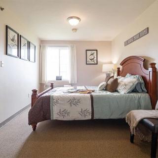 A cozy bedroom with a neatly made bed, decorative pillows, wall art, and a window letting in natural light.