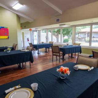 A spacious dining room with neatly arranged tables and chairs, featuring large windows and colorful artwork on the wall.