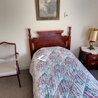 A cozy bedroom with a twin-sized bed, quilt, and classic wooden furniture.