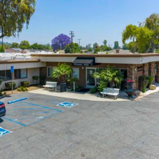 A small commercial building with a parking lot and greenery on a sunny day.