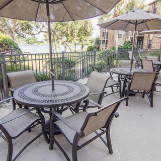 An outdoor patio area with tables and chairs under large umbrellas, enclosed by a fence.