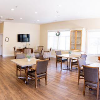 A bright dining area with several tables, chairs, a television, and wooden flooring.
