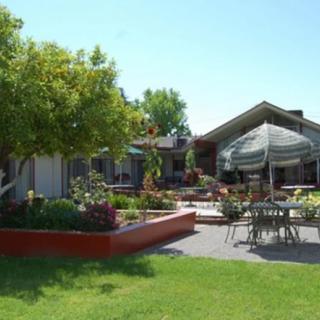 A spacious backyard with a patio area, outdoor furniture, and a large umbrella surrounded by lush greenery and well-maintained gardens.