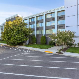 A modern building with large windows and a parking lot, surrounded by greenery.