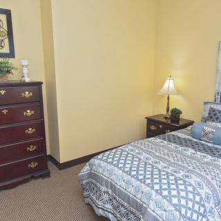 A cozy bedroom with a wooden dresser, bedside table, and patterned bedding.