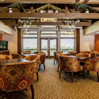 A cozy restaurant dining room with patterned chairs and tables, featuring large windows and a warm atmosphere.