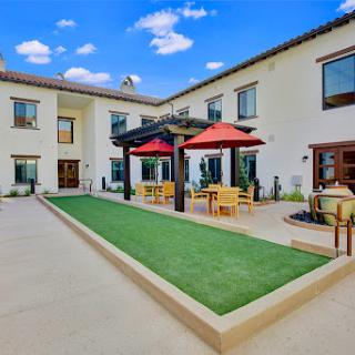 A serene outdoor courtyard featuring a modern design, with a green lawn and shaded dining areas under red umbrellas.