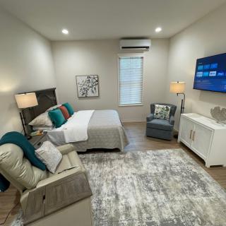 A modern and cozy bedroom with stylish decor, featuring a bed, armchair, lamps, and a wall-mounted television.