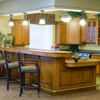 A modern kitchen with wooden cabinets, a large central countertop, bar stools, and stylish lighting.
