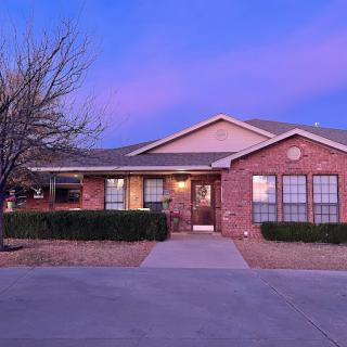 A brick house with a driveway and shrubs at sunset.