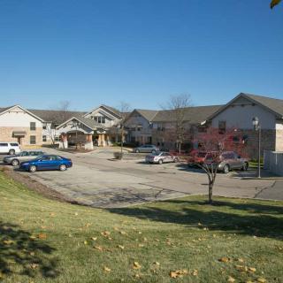 A view of a building complex with a parking lot and cars, surrounded by grass and trees under a clear blue sky.