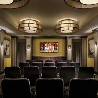 A cozy home theater setup with rows of comfortable seating facing a large screen, surrounded by elegant lighting fixtures.