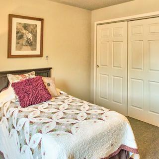 A cozy bedroom with a single bed and decorative pillows, featuring wall art and closet doors.