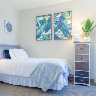 A modern bedroom featuring a neatly made bed, minimalist decor, and abstract artwork on the wall.