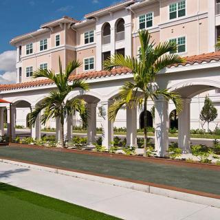 A sunny view of a multi-story building with palm trees lining a walkway.