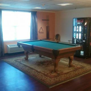 A cozy recreation room featuring a billiards table on a decorative rug, with a vending machine in the corner.