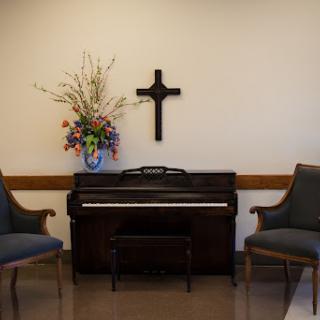 A serene corner with a piano, floral arrangement, and a cross for reflection.