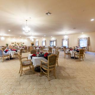 A spacious dining area with tables and chairs, softly lit by chandeliers, filled with people enjoying a meal.