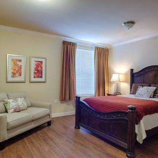 A cozy bedroom featuring a large bed with red bedding, a beige couch, and warm lighting.