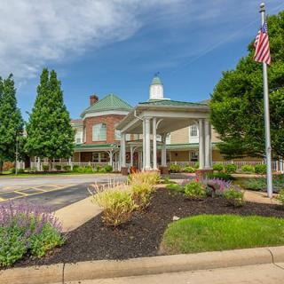 An entrance to a large building with a landscaped garden and flagpole on a clear day.