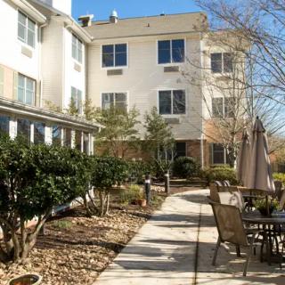 A sunny pathway leading through a landscaped outdoor area with tables and chairs.