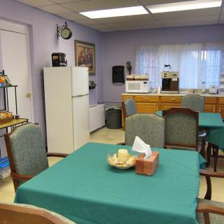 A cozy dining area with tables and chairs, featuring a refrigerator and microwave in the background.