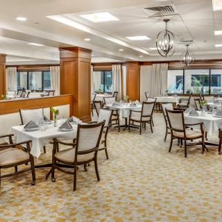 An elegant restaurant dining room with neatly arranged tables and chairs, featuring a chandelier and carpeted flooring.