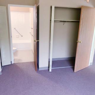 An empty bedroom with an open closet and a bathroom entrance.